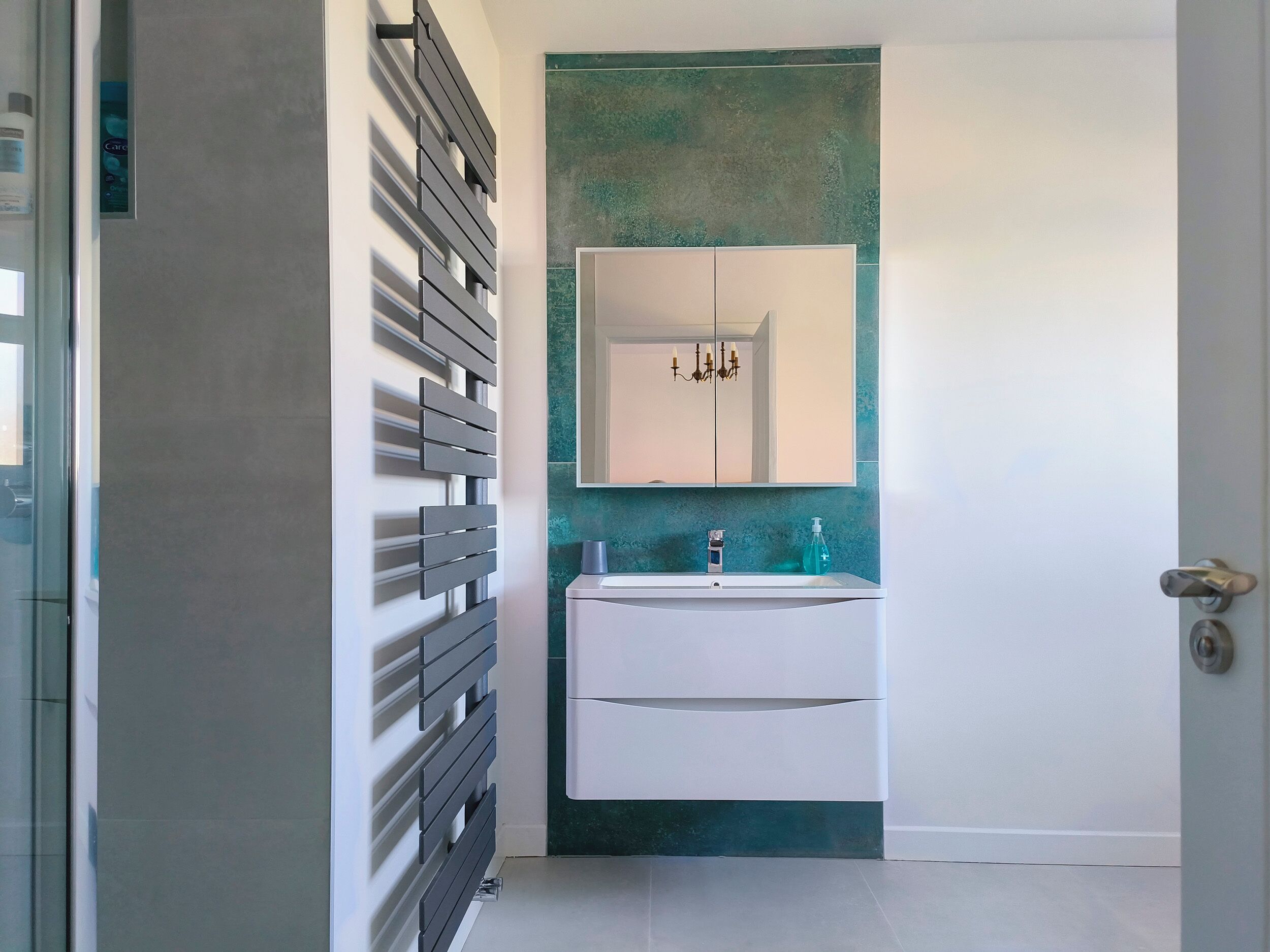 Un baño moderno con tocador blanco, pared de acento verde y lámpara colgante.