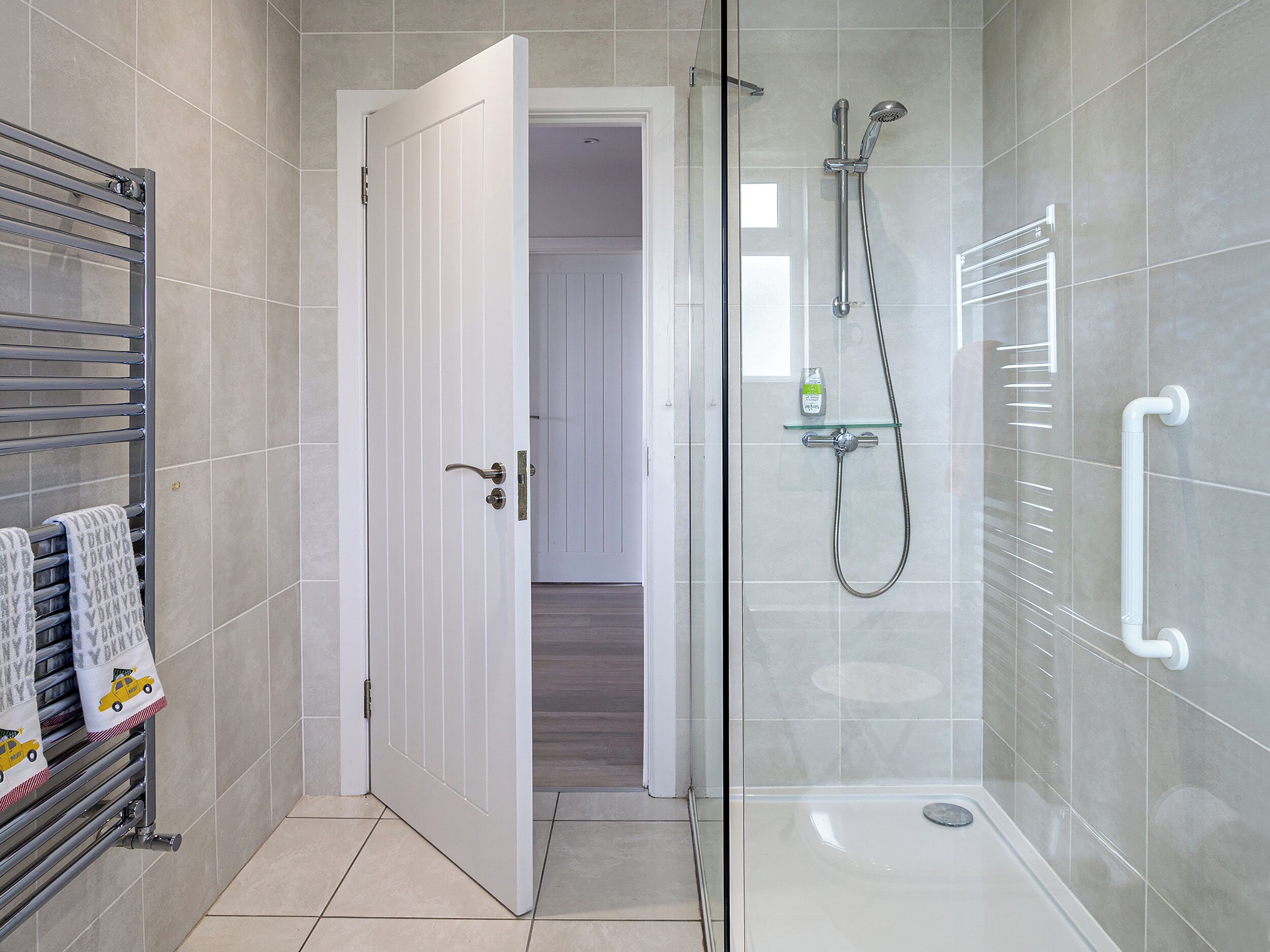 A modern bathroom with a glass shower enclosure, a white door, and a towel rack with towels.