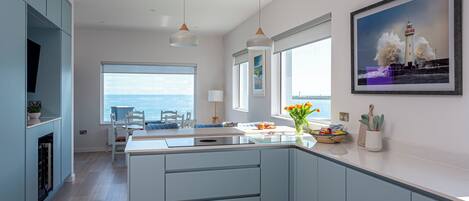 A modern kitchen with a central island, light blue cabinetry, and a view of the sea.