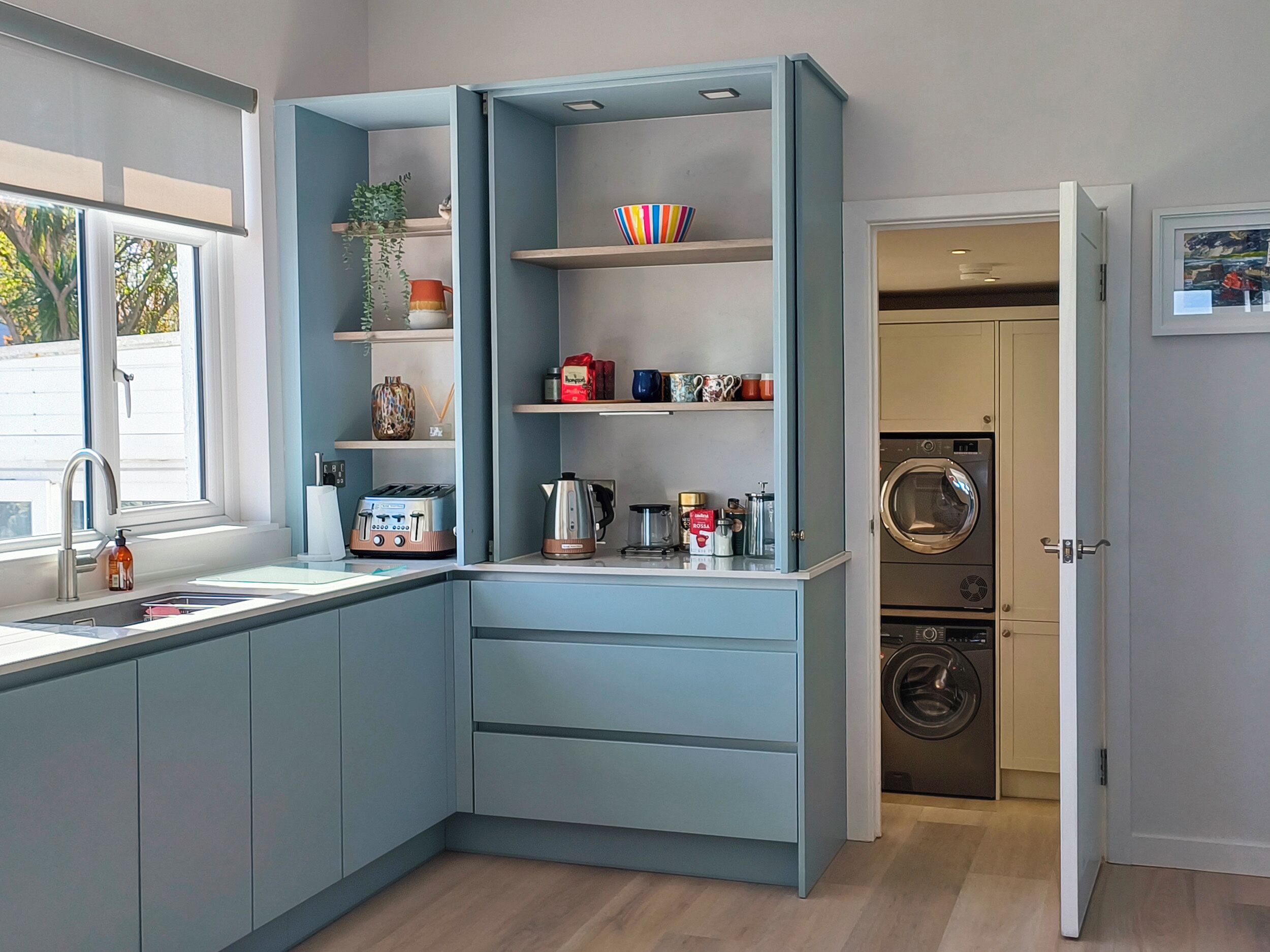 A compact kitchen with a built-in washing machine, a window with a view, and a sink with a faucet.
