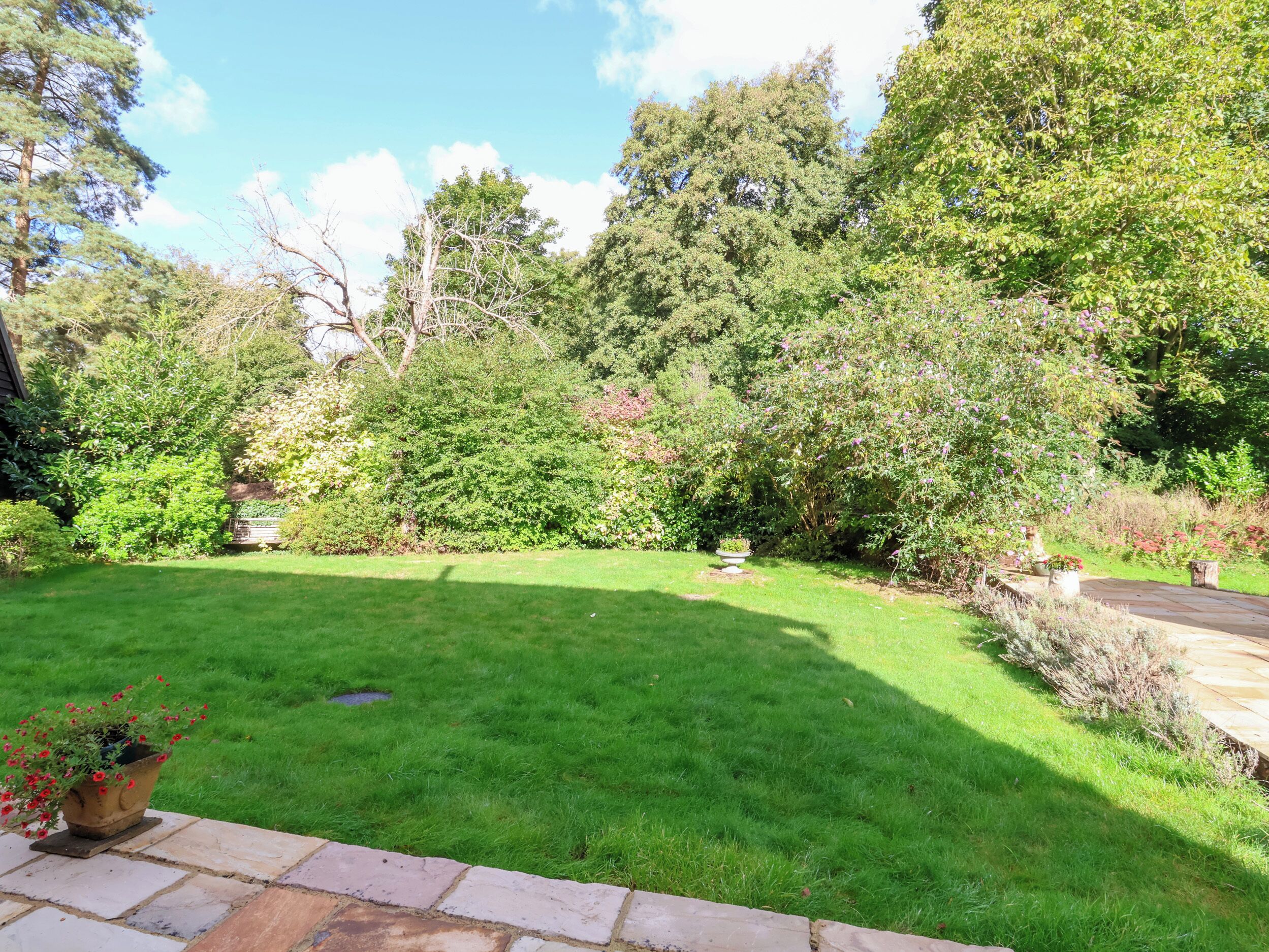 A well-maintained garden with a variety of trees and shrubs, a stone pathway, and a grassy lawn.