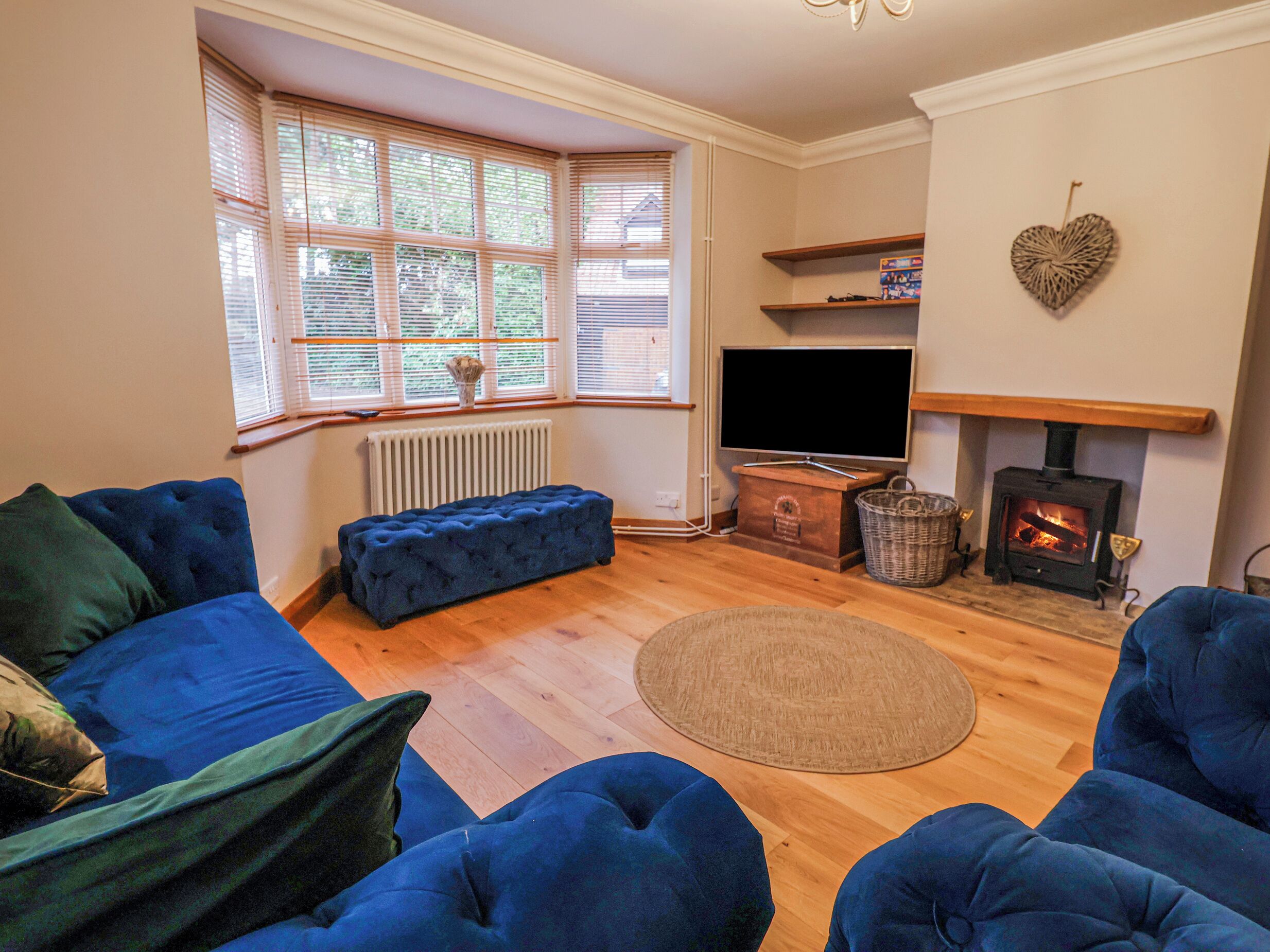 Ein Wohnzimmer mit blauem Sofa, Fernseher, Kamin und einem Fenster mit Jalousien.