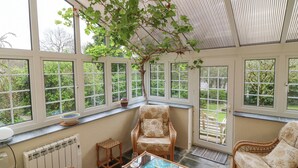 Um solário com móveis de vime, um tabuleiro de xadrez e uma grande janela com vista para um jardim.