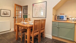 A dining area with a wooden table and chairs, a kitchen with a microwave and toaster, and a map on the wall. - Lavender Cottage (Coniston)