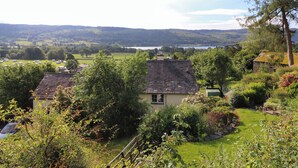A rural landscape with a house surrounded by lush greenery and a view of rolling hills in the distance. - Lavender Cottage (Coniston)