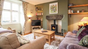 A cozy living room with a fireplace, comfortable seating, and a television. - Lavender Cottage (Coniston)