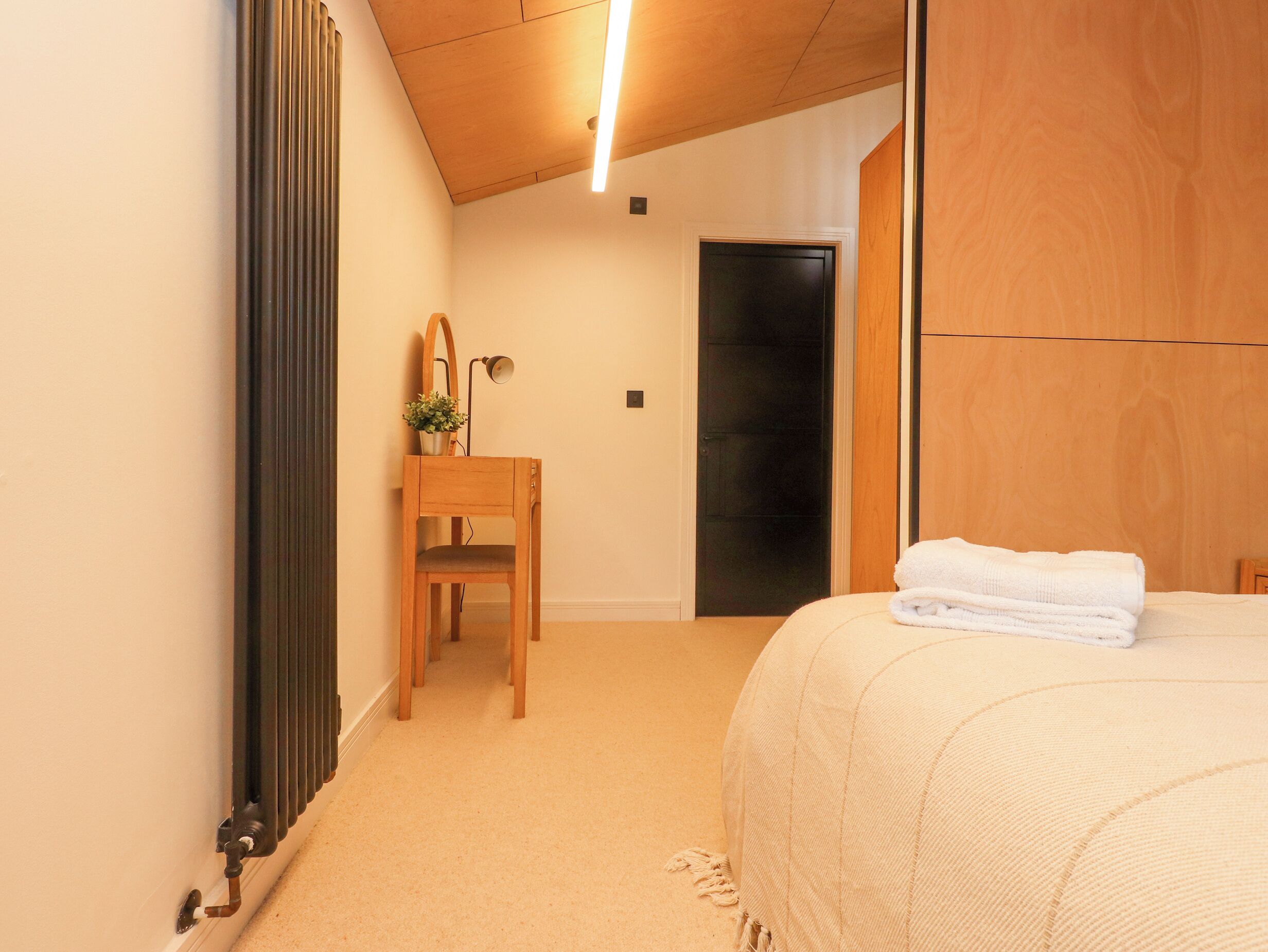 Un dormitorio con cama, una silla de madera, un radiador, un espejo y una puerta.