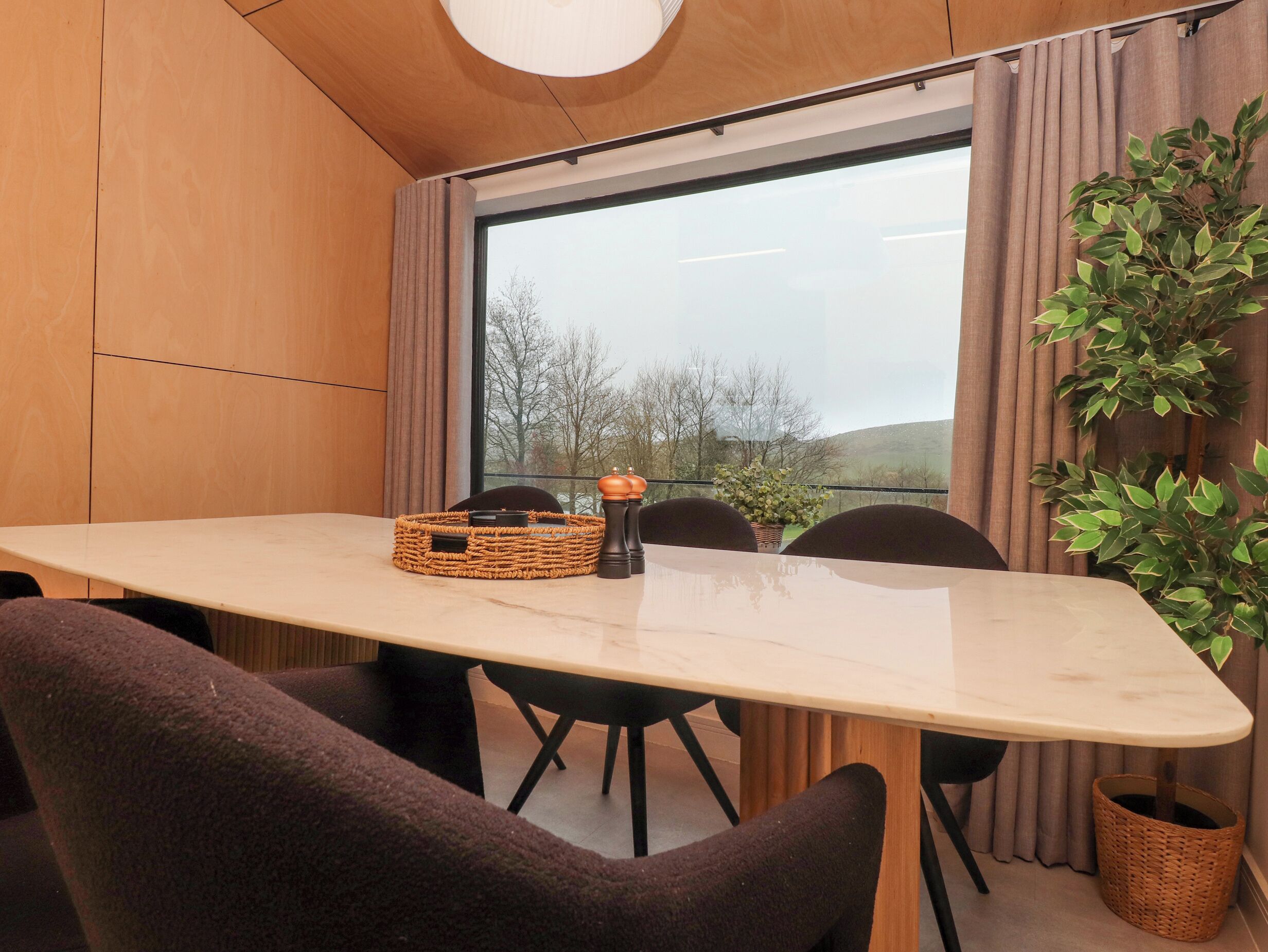 Quarto moderno com uma janela grande, teto de madeira, mesa com cadeiras e um cesto sobre a mesa.