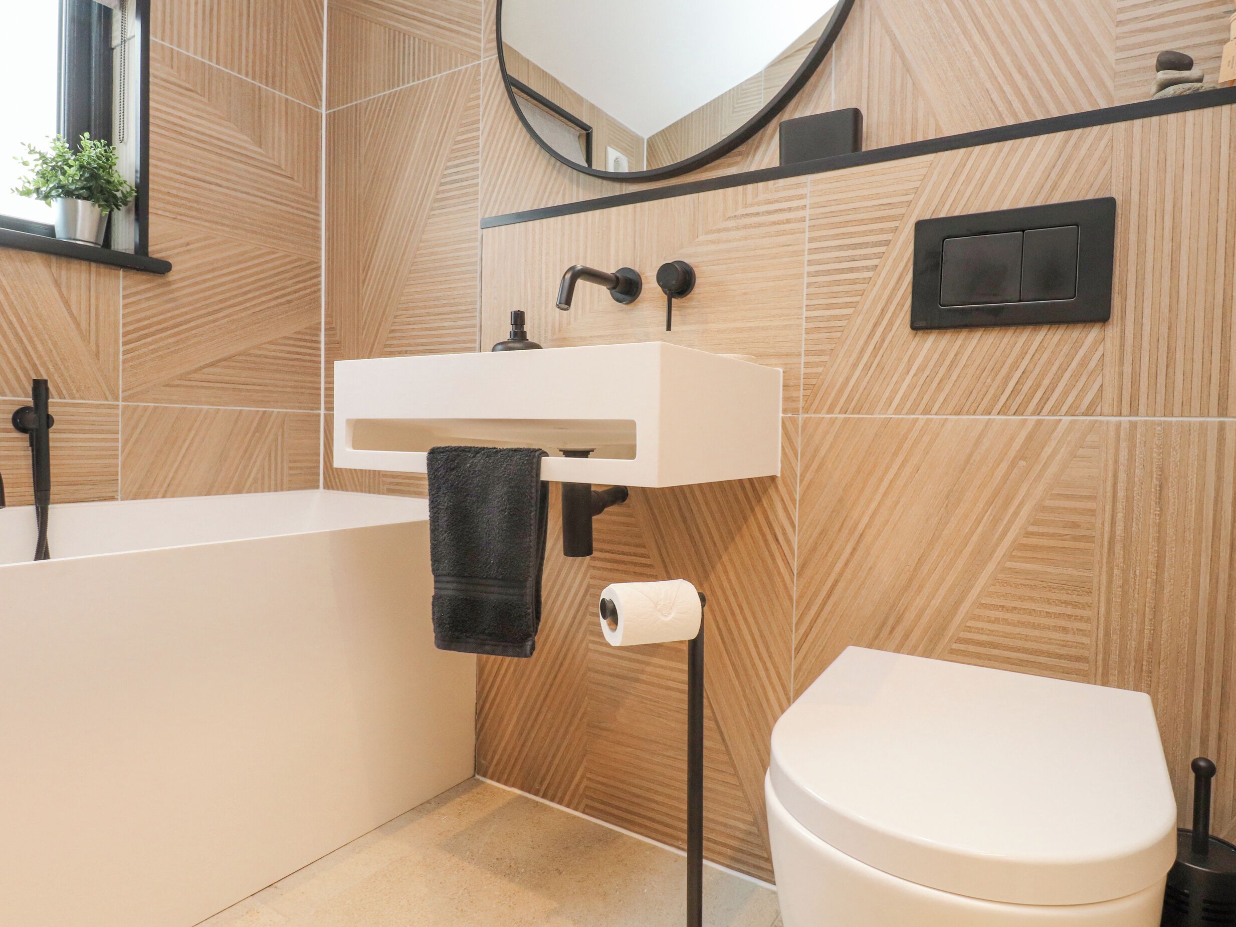 A modern bathroom with a freestanding bathtub, a white sink with a black faucet, and a toilet.