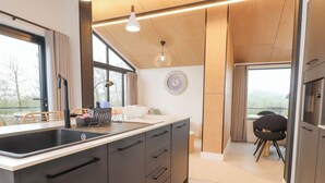 Une cuisine moderne dotée d’un grand îlot central, de meubles de rangement aux couleurs sombres et offrant une vue sur l’extérieur.