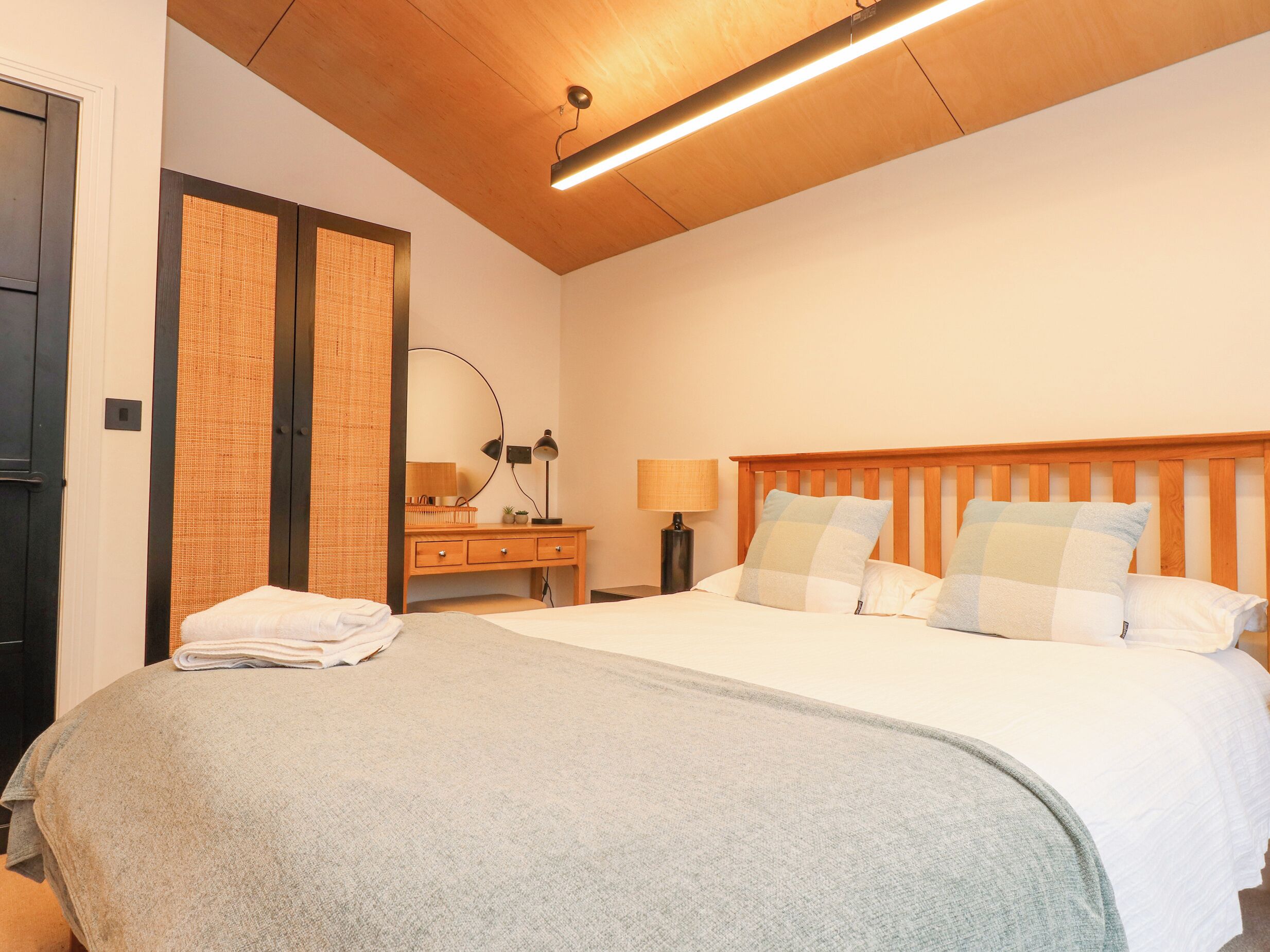 A bedroom with a bed, a desk, a mirror, and a nightstand.