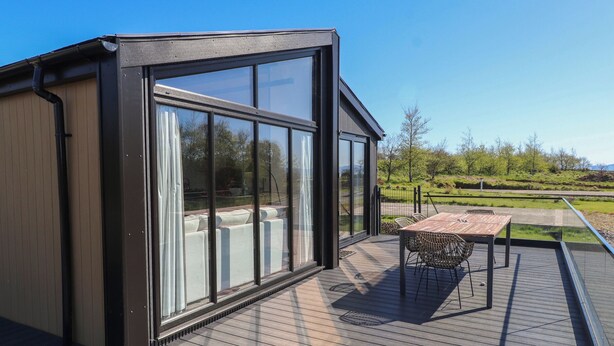 Un bâtiment moderne dot é de grandes fenêtres, d’une terrasse en bois et d’une table avec des chaises.