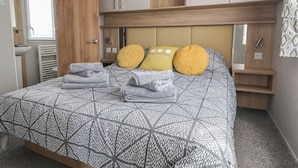 A bedroom with a bed, a wooden wardrobe, a mirror, and a window. - Woodlands Lodge (Ruthin)