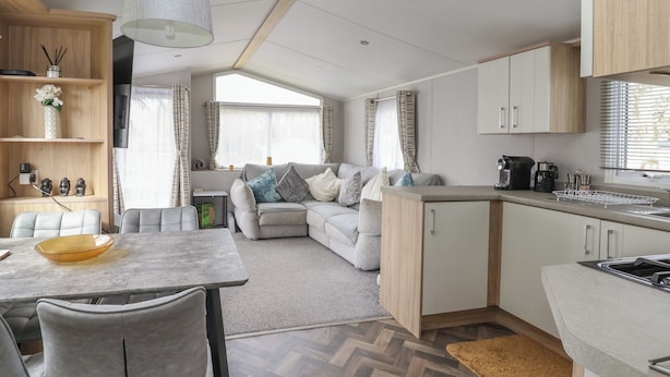 A modern kitchen with a dining area, a sofa, and a herringbone-patterned floor. - Woodlands Lodge (Ruthin)
