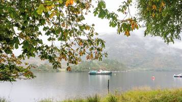 Un llac tranquil amb barques, envoltat d'arbres i muntanyes.