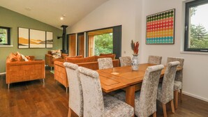 A dining area with a wooden table and six upholstered chairs, a sofa with orange cushions, and a vase with dried plants.