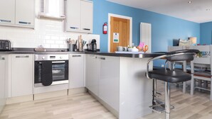 A modern kitchen with white cabinets, a built-in oven, and a coffee machine. - Flat 2 Niles Place (Padstow)