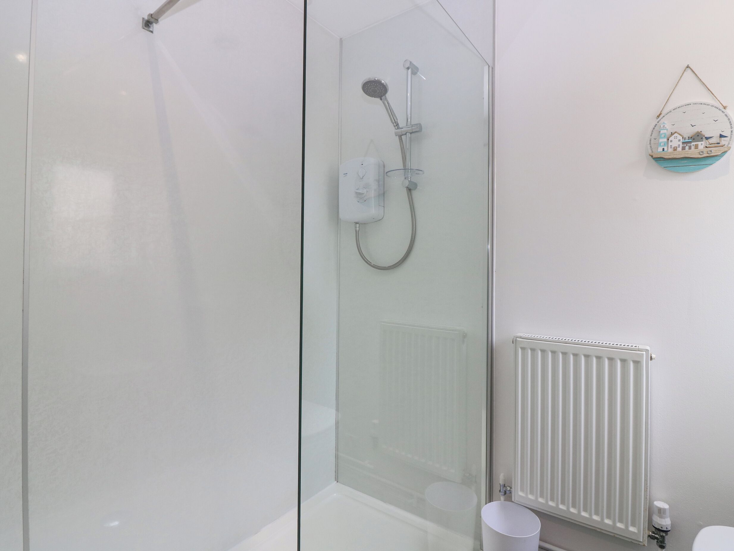 Ein modernes Badezimmer mit einer gläsernen Duschkabine, einem weißen Heizkörper und einem kleinen Waschbecken.