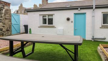 A patio area with a wooden table and benches, a small window, and a door.