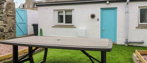 Un patio con una mesa y bancos de madera, una ventana pequeña y una puerta.
