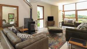 Un salón espacioso con techo alto, chimenea, televisor y ventanas amplias que ofrecen vistas al exterior.