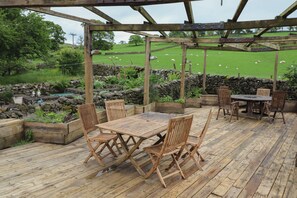 A wooden deck with a pergola, surrounded by stone walls and garden beds. - Beckside Hall (Carnforth)