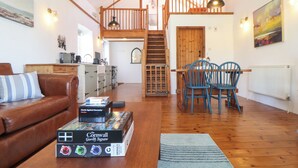 Uma sala de estar espaçosa com um sofá de couro marrom, uma mesa de jantar de madeira com cadeiras azuis e um jogo de quebra-cabeça na mesa de centro.