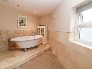 A bathroom with a freestanding bathtub, a cabinet, and a window. - Homestead (High Peak)