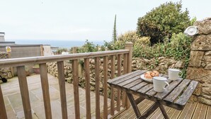 A wooden deck with a table set for two, overlooking a garden and the sea. - Fisherman's Cottage, King Street (Portland)