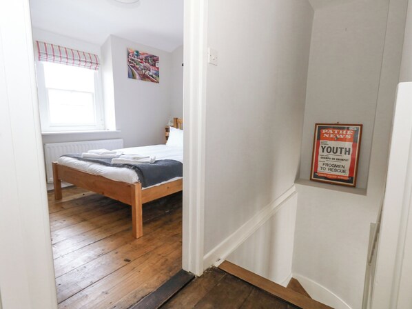 Quarto com cama de madeira, radiador, janela com persiana listrada e um cartaz na parede.
