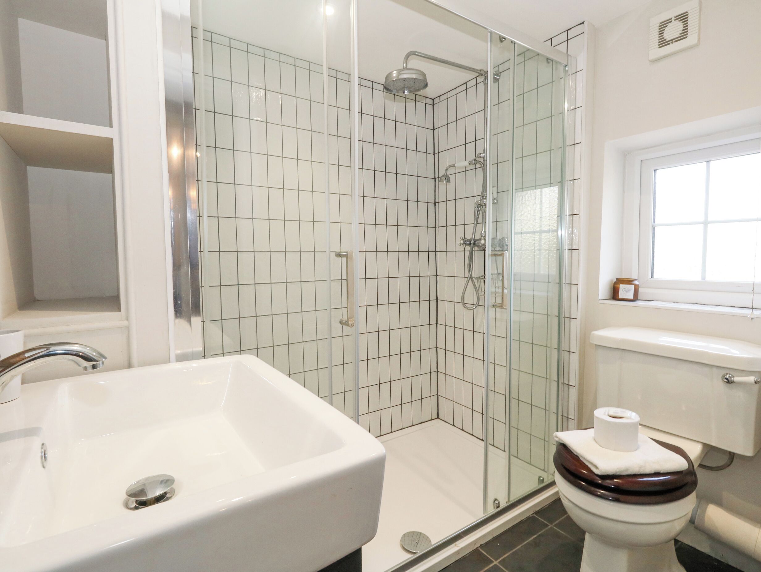 A bathroom with a white sink, a glass shower enclosure, and a toilet with a wooden seat.