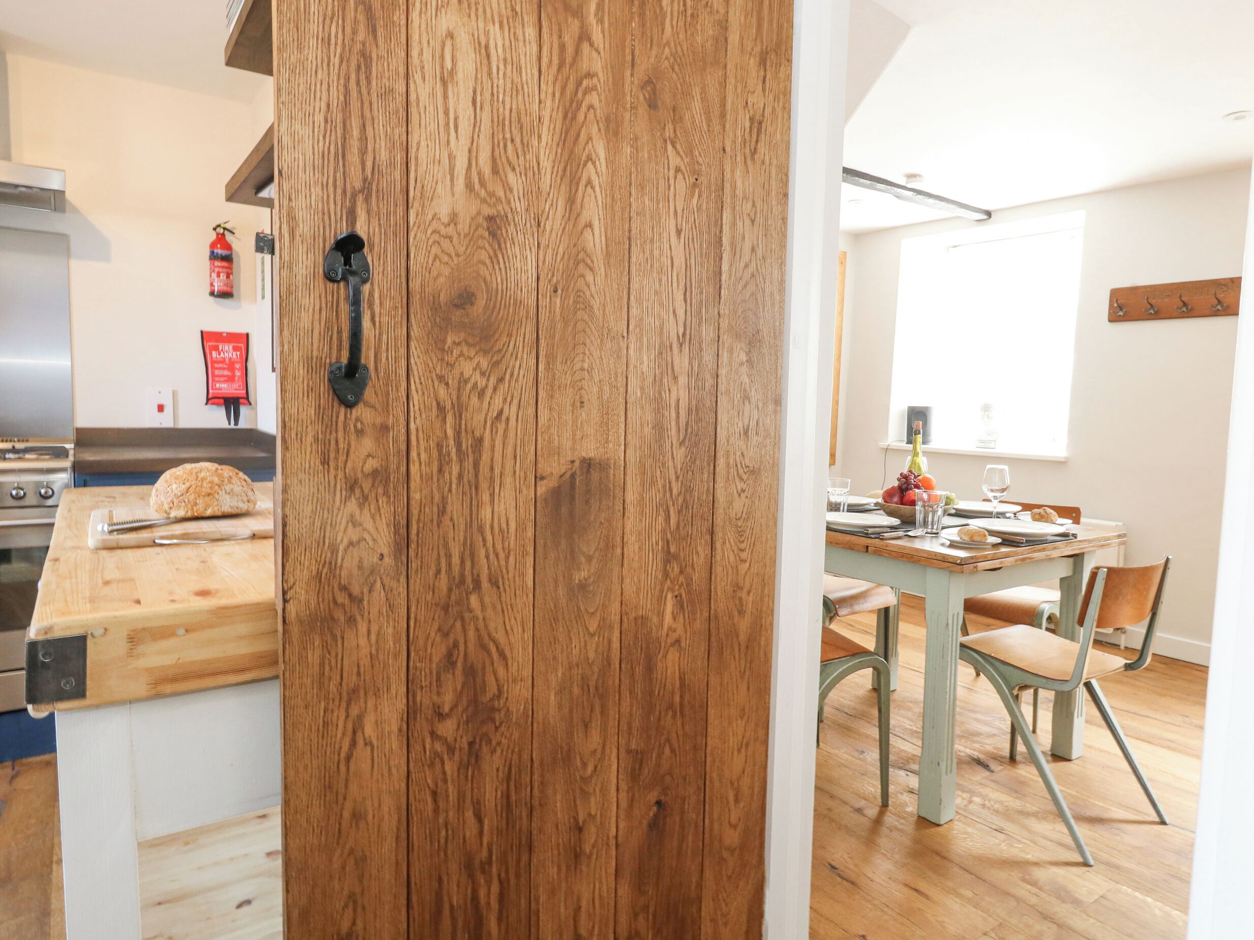 A kitchen with a wooden door, a cutting board with a loaf of bread, and a dining area with a table set for two.