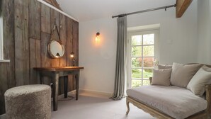 Een kamer met een rustieke houten wand, een ronde spiegel, een houten tafel, een comfortabele bank en een bed met hoofdeinde.