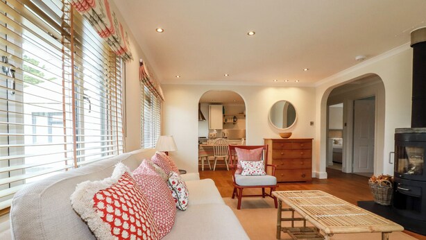 A living room with a sofa, a wooden table, and a fireplace. - 6 Trelawney Court (Wadebridge)