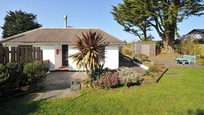 A small white building with a tiled roof, a wooden fence, and a large tree in the background. - 6 Trelawney Court (Wadebridge)