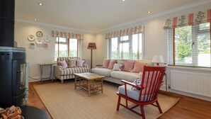 A cozy living room with a sofa, a chair, a coffee table, and a fireplace. - 6 Trelawney Court (Wadebridge)