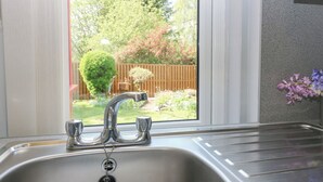 Eine Küche mit einer Spüle aus Edelstahl, einem Fenster mit Blick auf einen Garten und einer Vase mit Blumen auf der Arbeitsfläche.