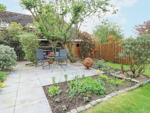 A patio with a table and chairs, surrounded by a garden with various plants and a wooden fence. - The Cottage (Kirriemuir)