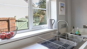 Eine Küche mit Fenster, einer Spüle, einem Obstkorb und einem dekorativen Gegenstand an der Fensterbank.