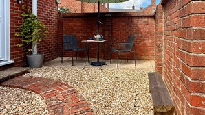 Eine Terrasse mit Tisch, Stühlen, einem Blumentopf und einem grünen Sonnenschirm.