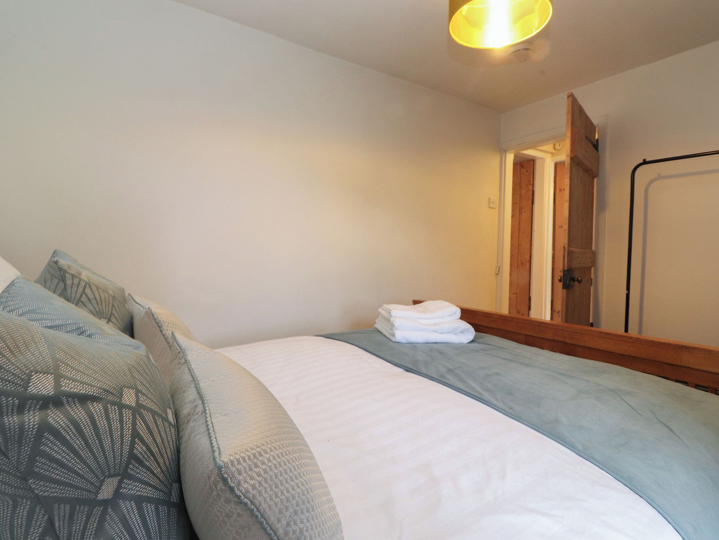 Een slaapkamer met een bed, kussens, een opgevouwen handdoek, een houten hoofdbord en een deur.