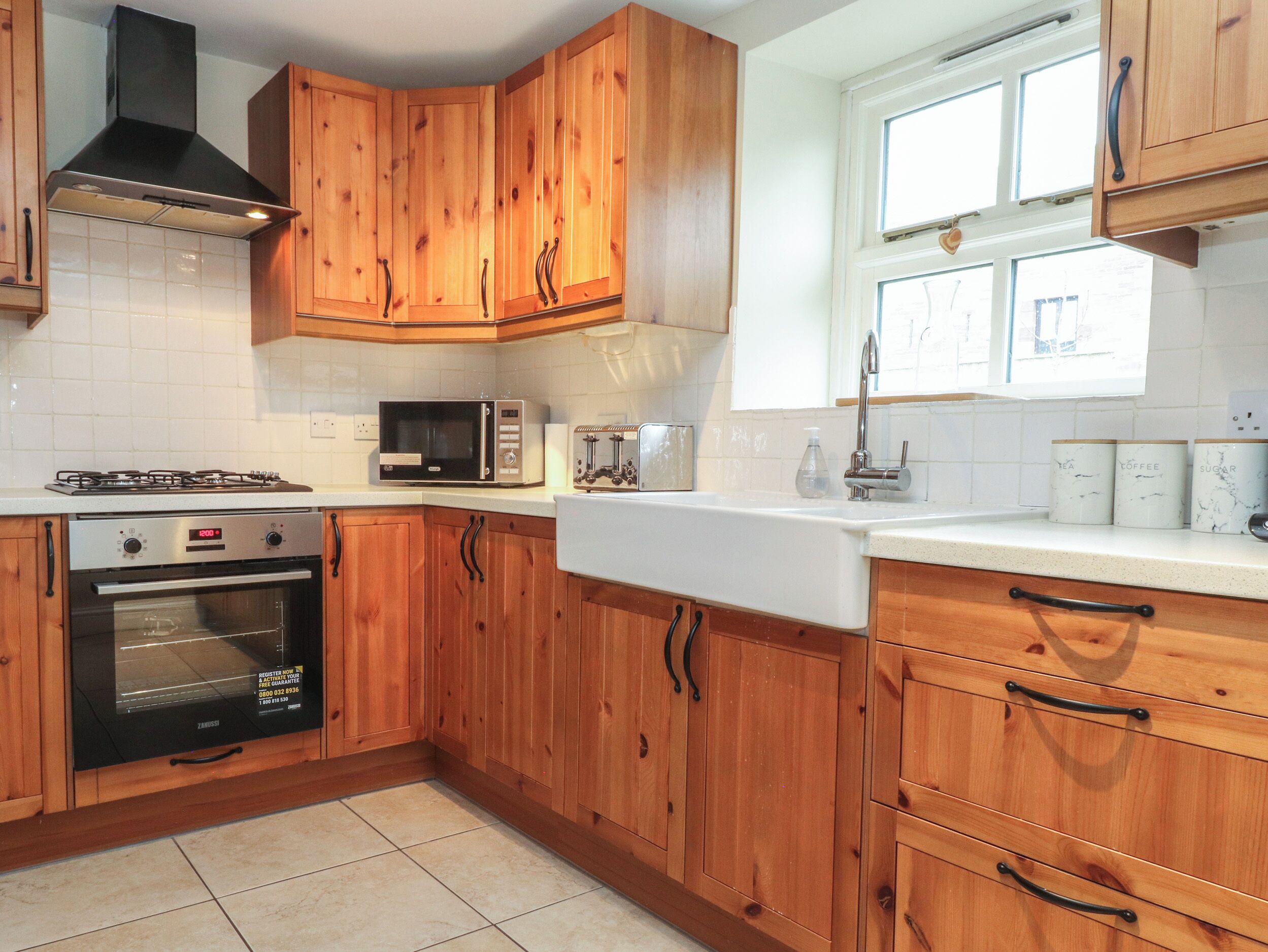 Una cocina con armarios de madera, microondas, tostadora, lavamanos y ventana con persianas.