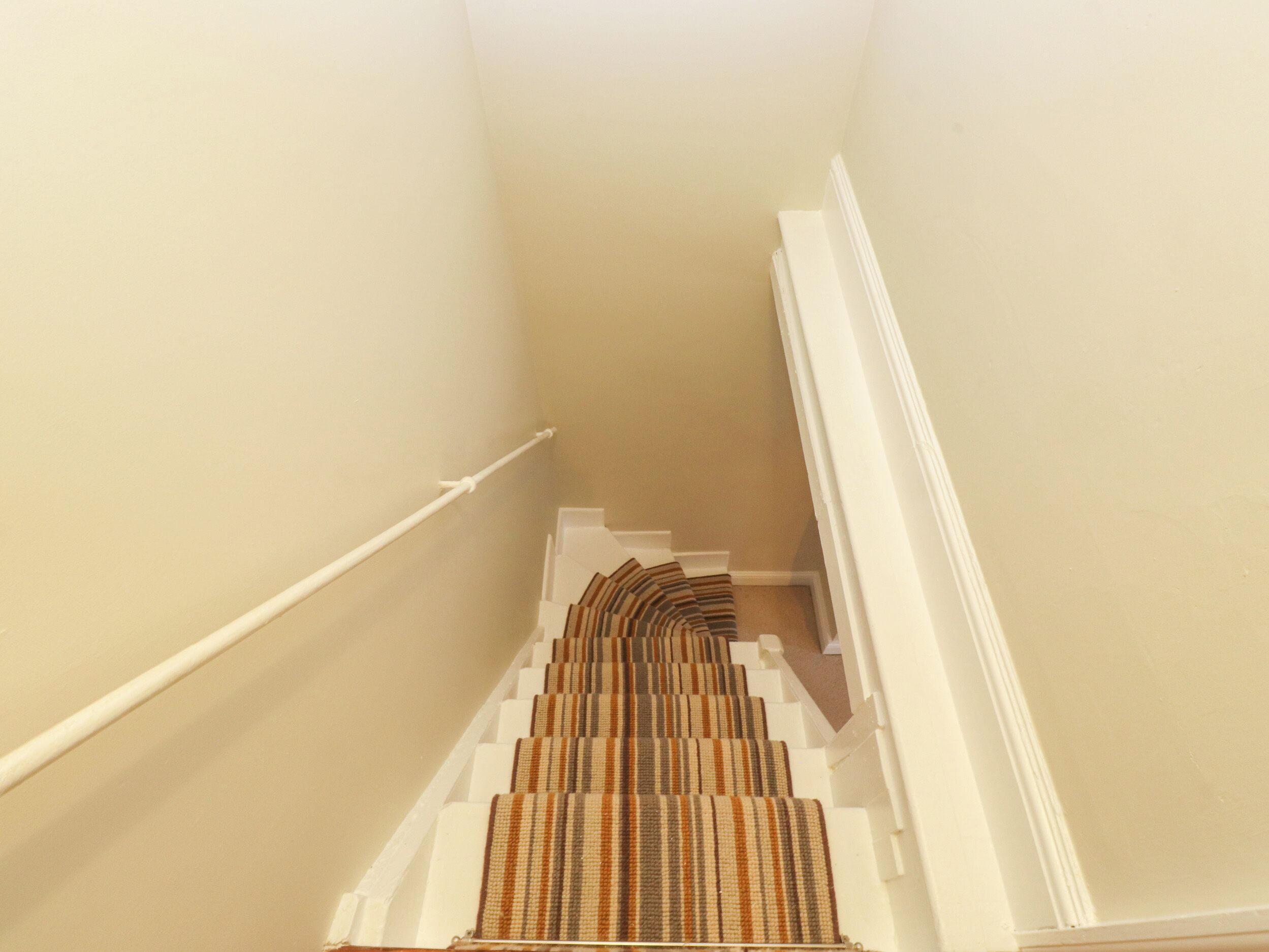 Eine Treppe mit einem Streifen Teppich und weißen Wänden.
