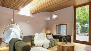 Een moderne woonkamer met een hangstoel, een groene bank en een ronde houten salontafel.