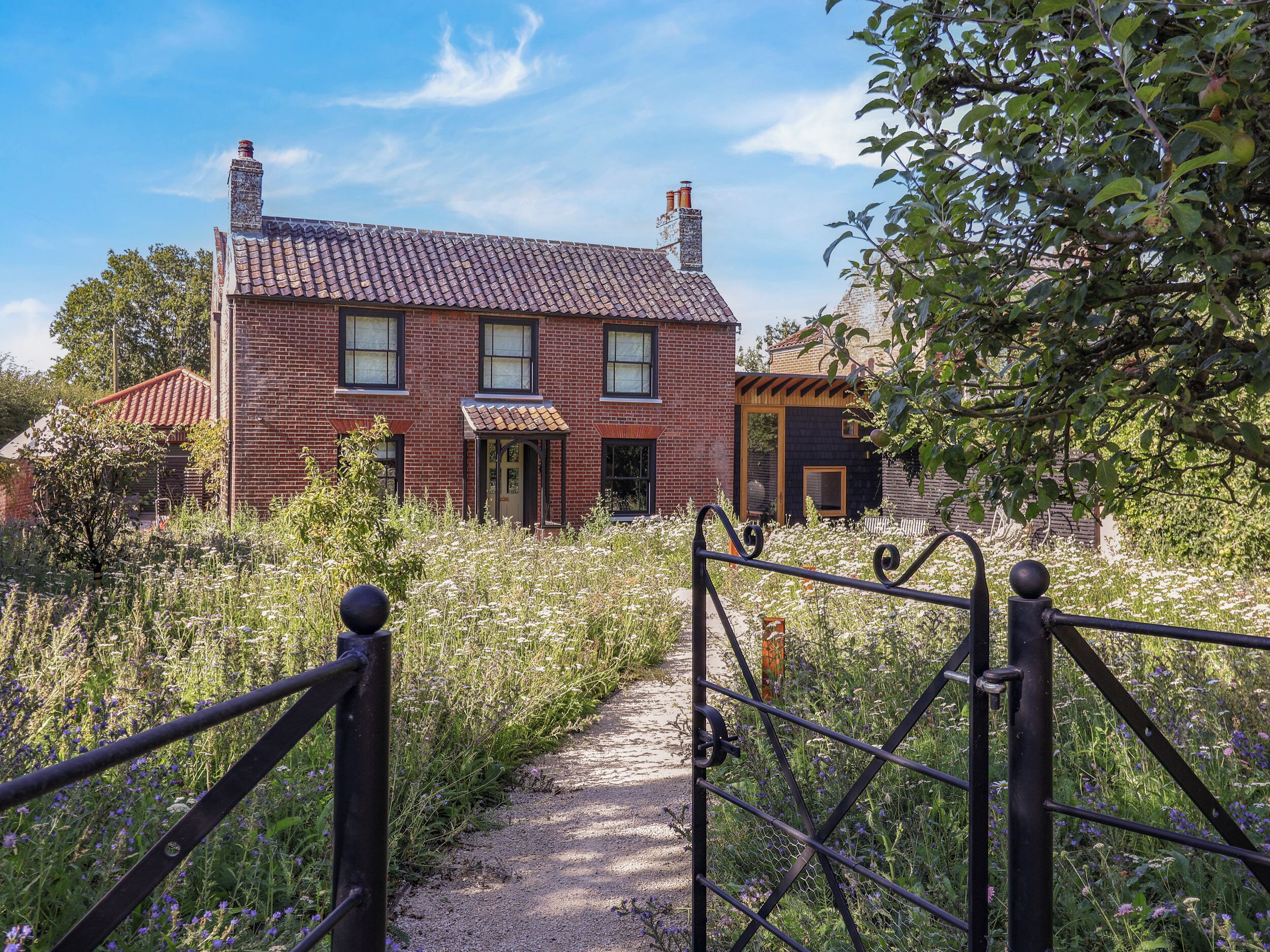 A brick house with a tiled roof, a wooden porch, and a garden path leading to a metal gate.