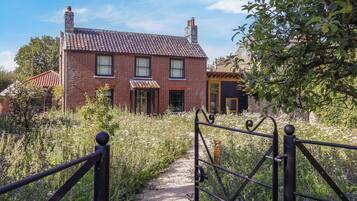 A brick house with a tiled roof, a wooden porch, and a garden path leading to a metal gate.
