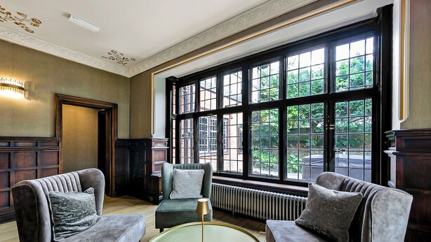 A room with two grey armchairs, a round table, and a large window with a view of greenery. - Tudor Grange (Bournemouth)