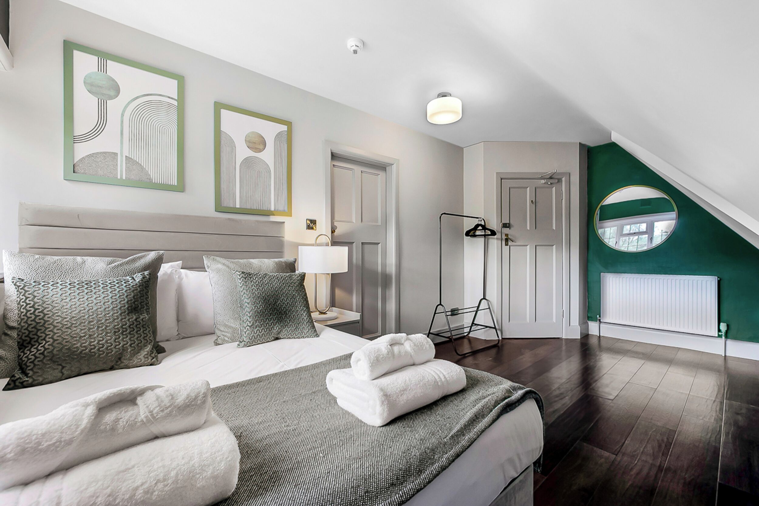 Un dormitorio moderno con cama, almohadas, mesita de noche, lámpara, lámpara de pie y espejo.