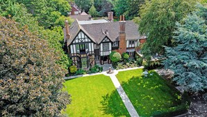A Tudor-style house with a well-maintained lawn and a central garden feature. - Tudor Grange (Bournemouth)