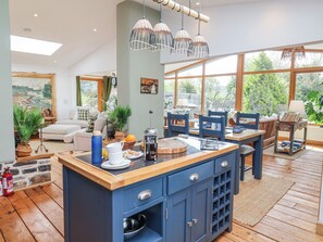 A modern kitchen with a blue island, wooden flooring, and large windows offering a view of greenery.